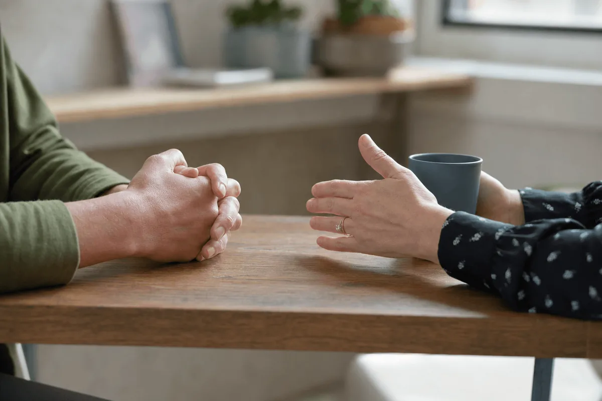 A close-up of two people's hands resting on a table during a supportive counseling conversation