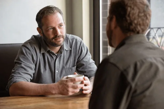 Two people sitting and talking over coffee in a quiet, supportive one-on-one conversation